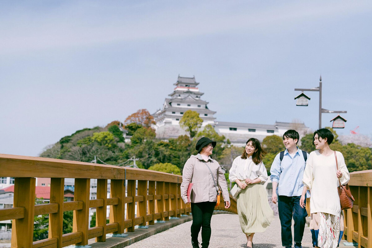 女性ガイドとともに唐津城を散策する3人の男女